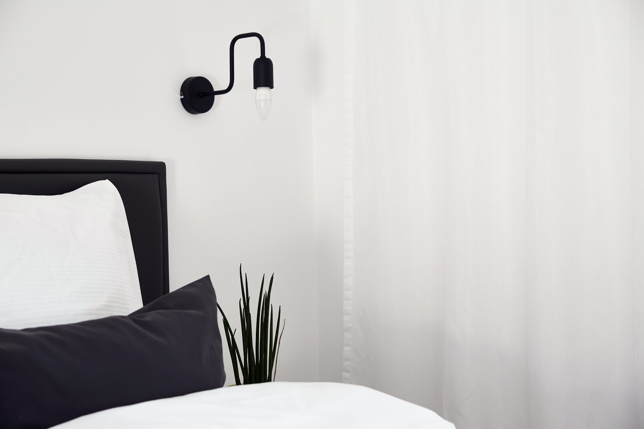 A neatly made bed with white and black bedding, a black headboard, and a wall-mounted light fixture.