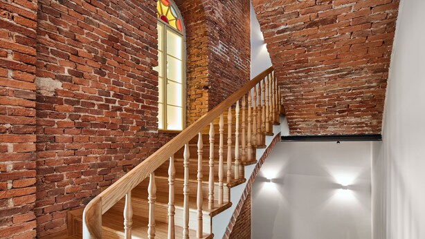 Una escalera de madera con un lateral de pared de ladrillo y otro de pared blanca.