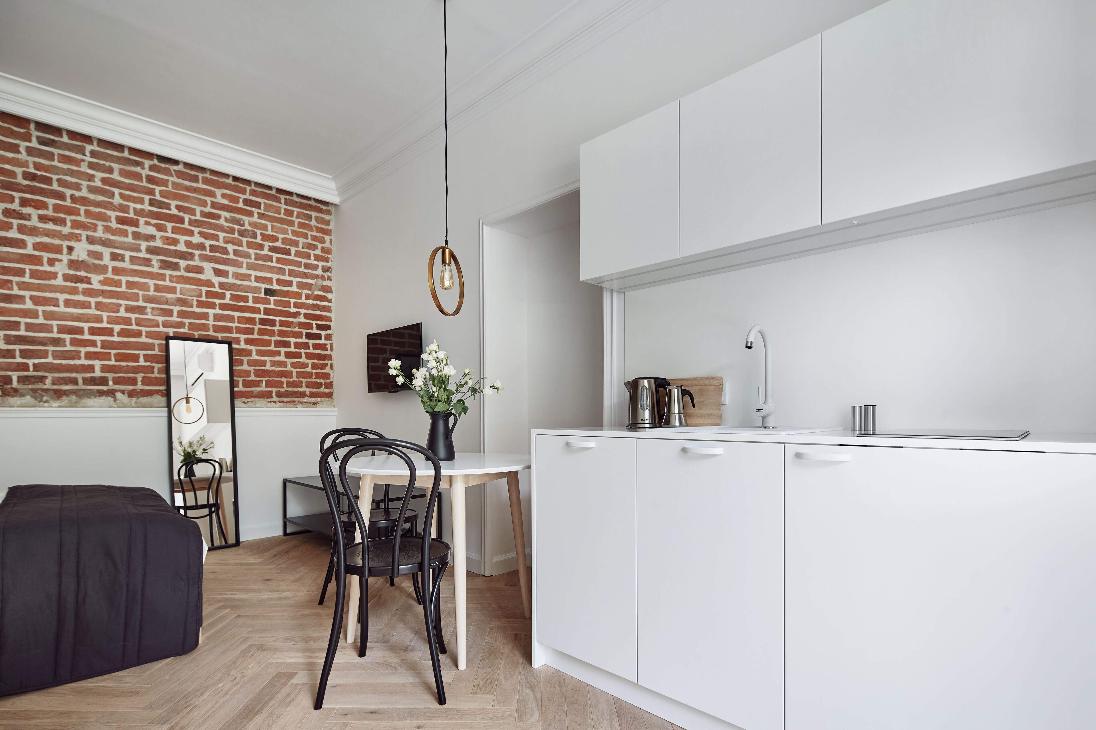 A modern kitchen with white cabinets, a brick accent wall, a dining area with a table and chairs, and a black ottoman.
