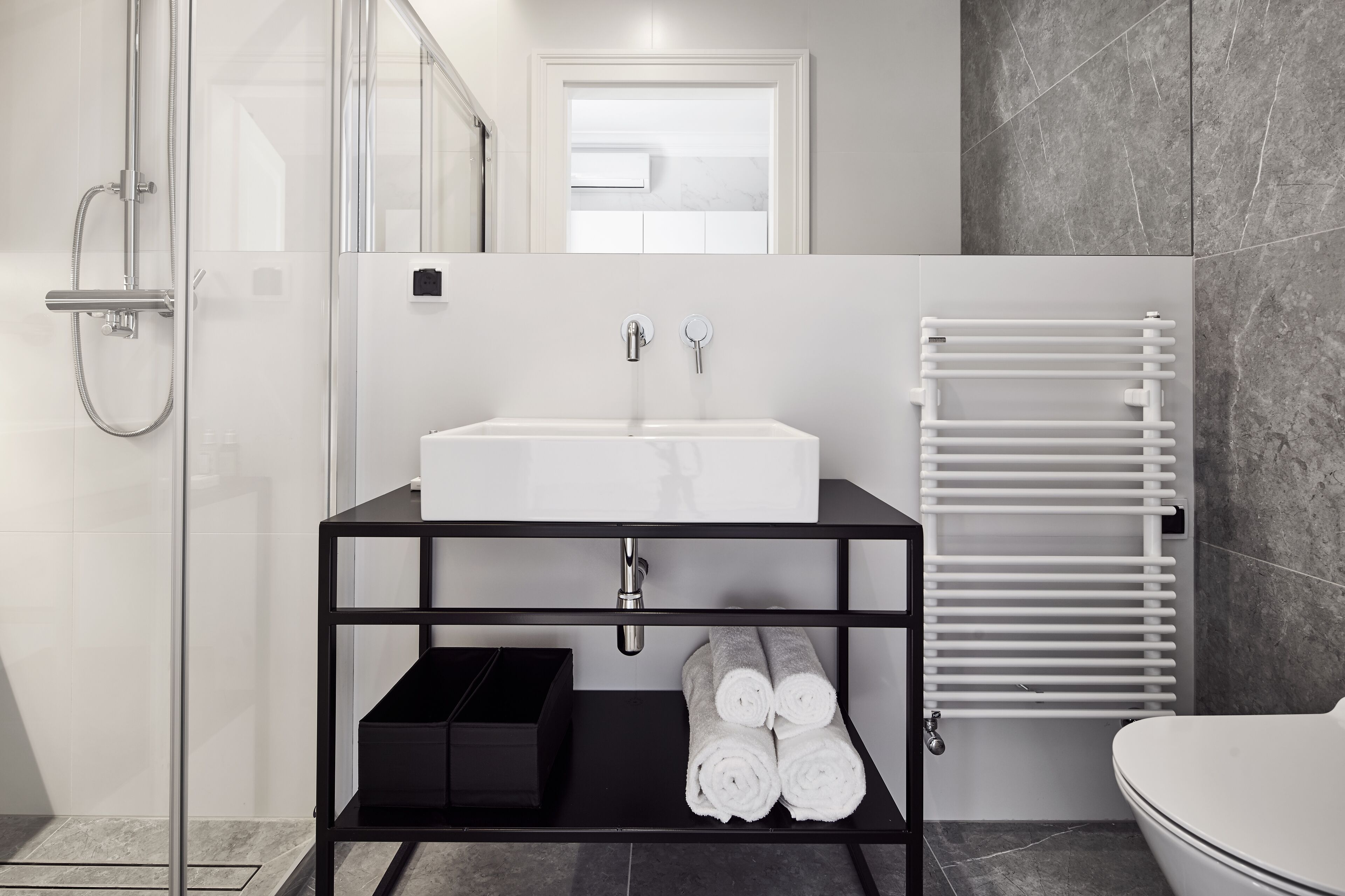 Une salle de bain moderne avec un lavabo blanc, des étagères noires et un porte-serviettes blanc.