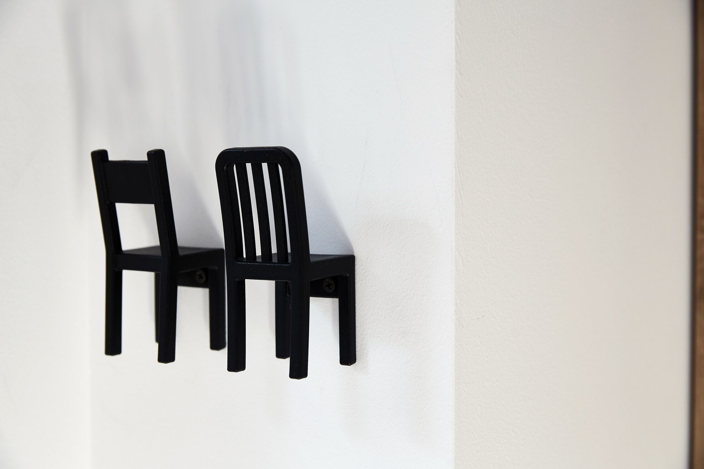 Two black chairs mounted on a white wall.