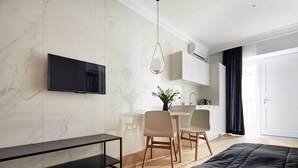 Una habitación de hotel moderna con una televisión de pantalla plana montada en la pared, una zona de comedor con mesa y sillas, un banco negro y una cama grande.
