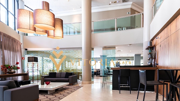 Een ruime lobby met een modern ontwerp, met een zithoek met banken en een salontafel, een bar met krukken, en een grote decoratieve letter 'Y' aan de muur.