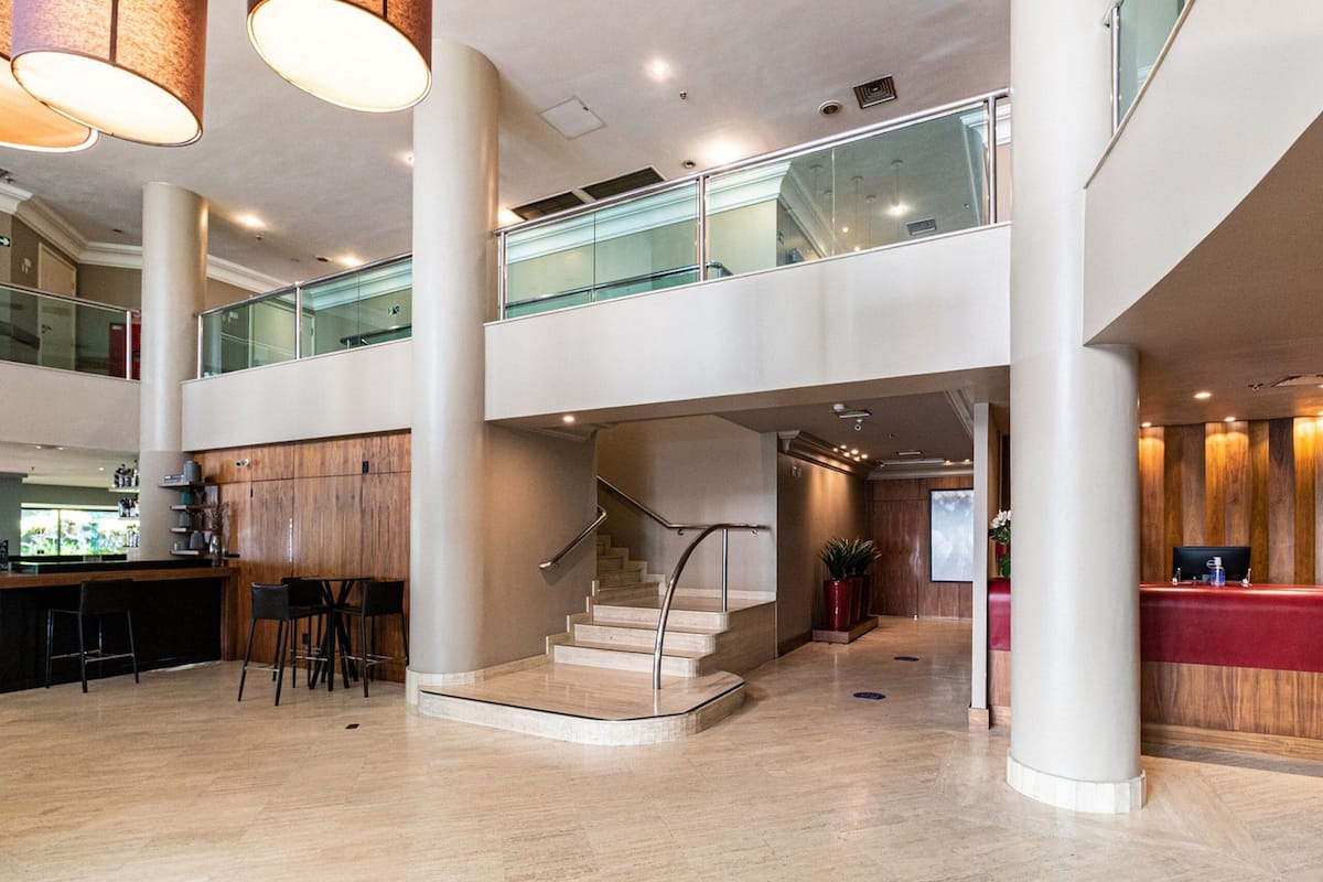 Um hall amplo com uma escadaria moderna, um balcão de recepção e um espaço de bar.