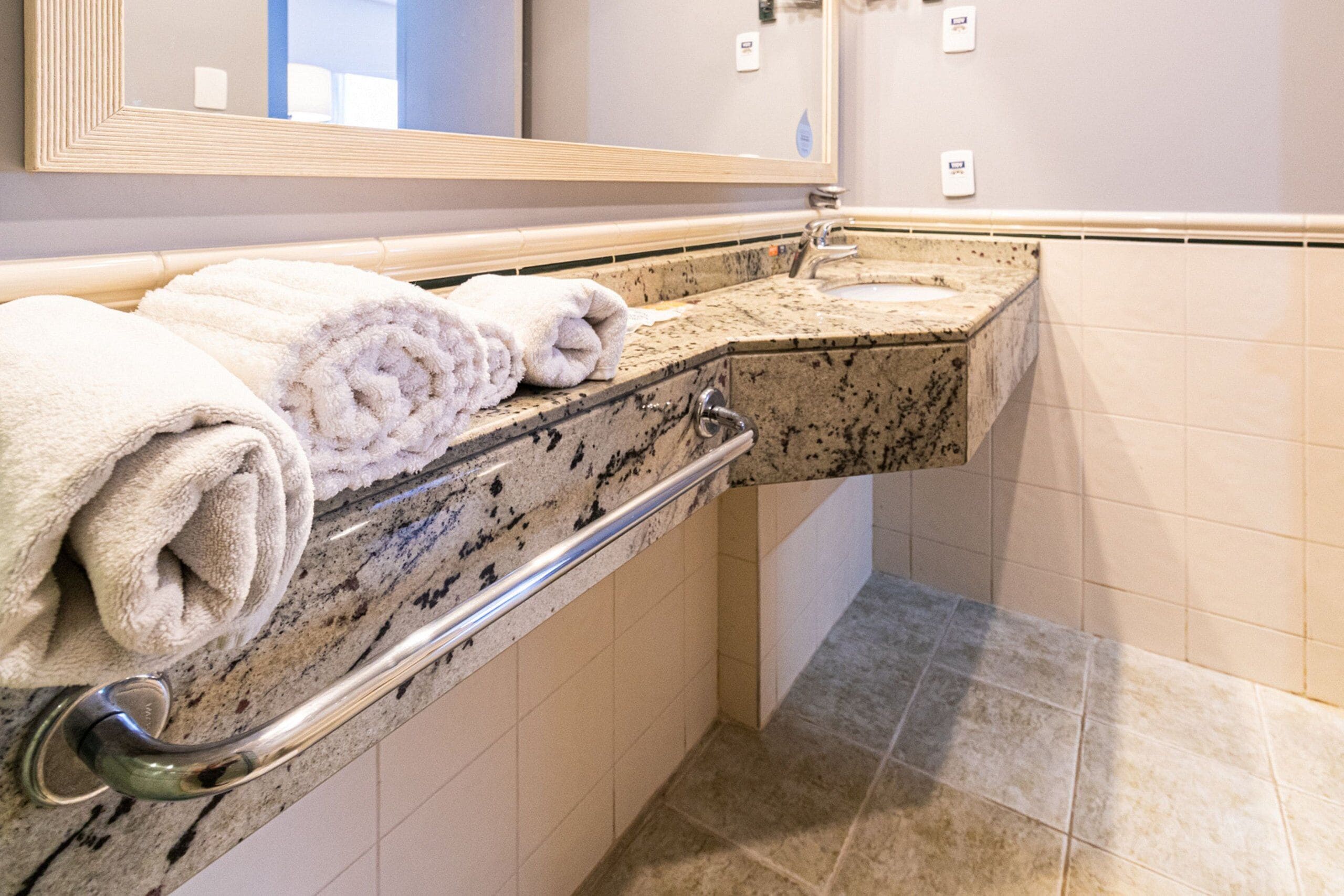 Un baño con encimera de granito, lavamanos, espejo y toallero con toallas.