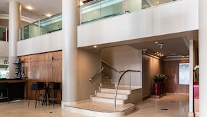 Een moderne hotel lobby met een centrale trap, een bar en een zithoek.