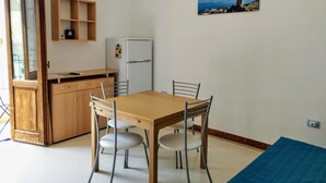 A compact kitchen with a wooden table and chairs, a white refrigerator, and a small shelf unit. - Appartamenti Blu Mare "SCOPELLO" situeted in a strategic position (Castellammare del Golfo)