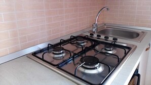 A kitchen with a gas stove, a sink, and a backsplash of pink tiles. - Appartamenti Blu Mare "SCOPELLO" situeted in a strategic position (Castellammare del Golfo)