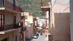 A narrow street with buildings on both sides, a clear blue sky, and a hilly landscape in the background. - Appartamenti Blu Mare "SCOPELLO" situeted in a strategic position (Castellammare del Golfo)