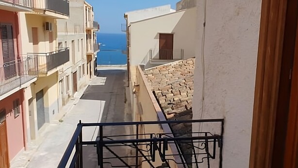 A narrow street with buildings on both sides, a stone wall on the right, and a view of the sea in the distance. - Appartamenti Blu Mare "SCOPELLO" situeted in a strategic position (Castellammare del Golfo)