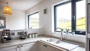 Eine moderne Küche mit weißen Schränken, einer doppelten Spüle, einer Kaffeemaschine und einem Fenster mit Blick ins Grüne.