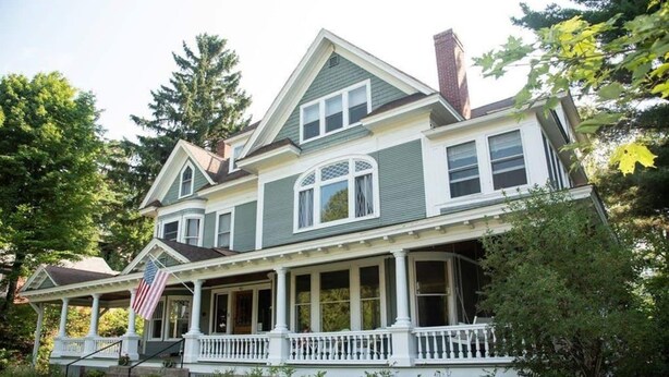 A large, two-story house with a wrap-around porch, a chimney, and a flag on the front. - Franklin Manor Bed & Breakfast (Saranac Lake)