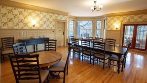 A dining area with a round table and multiple chairs, a kitchen with white cabinets, and a bay window with a view. - Franklin Manor Bed & Breakfast (Saranac Lake)