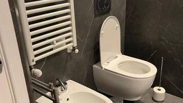 Un bagno moderno con due bidet, un water, un portasciuga e un dispenser per carta igienica.