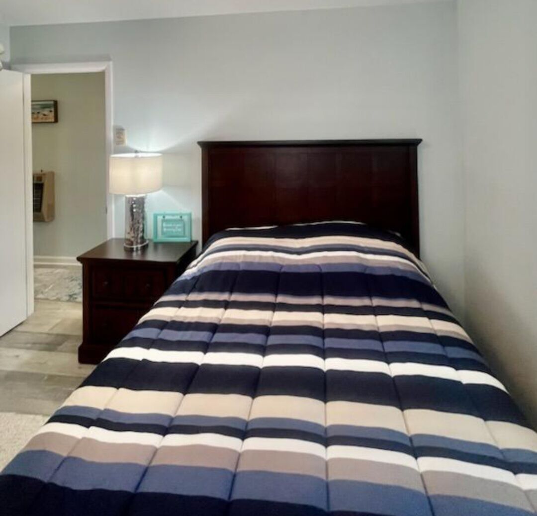 Quarto com cama, mesa de cabeceira e abajur.