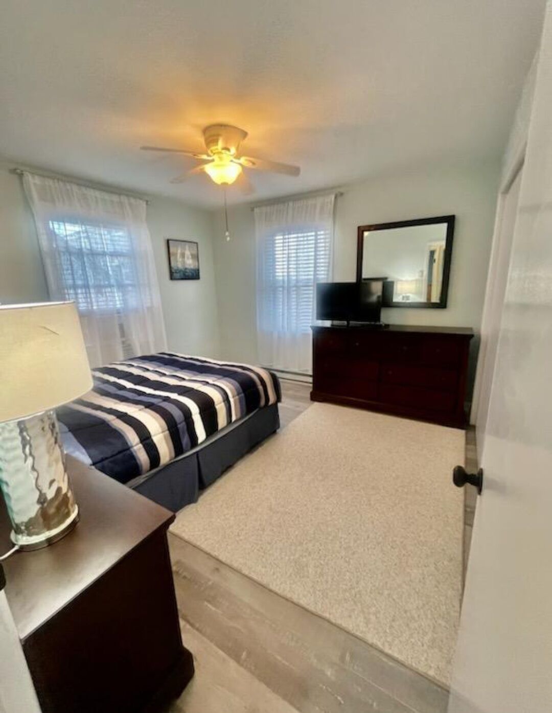 A bedroom with a bed, a dresser, a ceiling fan, and a window with blinds.