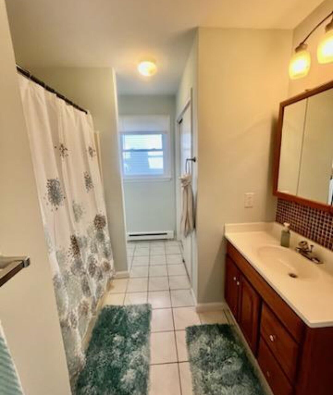 Une salle de bain avec un rideau de douche, un lavabo, un miroir et un sol carrelé.