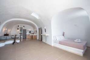 A spacious room with a large bed, a seating area, and a kitchen. - Iatis View Collection (Santorini)