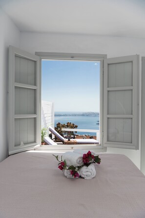 A room with a bed, a view of the sea, and a balcony with a table and chairs. - Iatis View Collection (Santorini)