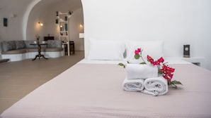 A hotel room with a bed, a bedside table, a nightstand, a lamp, a sofa, and a staircase leading to an upper level. - Iatis View Collection (Santorini)