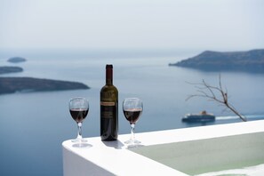A bottle of wine and two glasses on a balcony overlooking a body of water with a boat in the distance. - Iatis View Collection (Santorini)