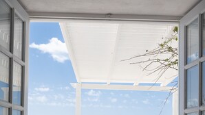 An open balcony with a view of the sea and mountains, a white ceiling, and a black object on the floor. - Iatis View Collection (Santorini)
