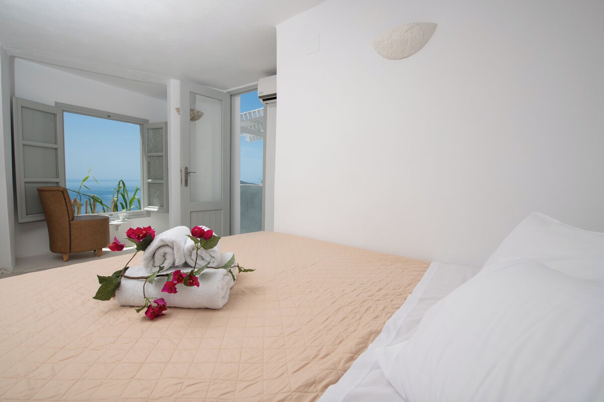 Een hotelkamer met een bed, een stoel, een raam met uitzicht en een deur naar een balkon.