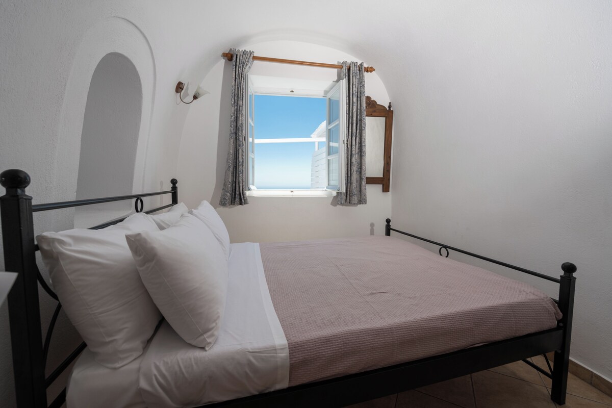 Una cama individual con ropa de cama blanca en una habitación con ventana y espejo.