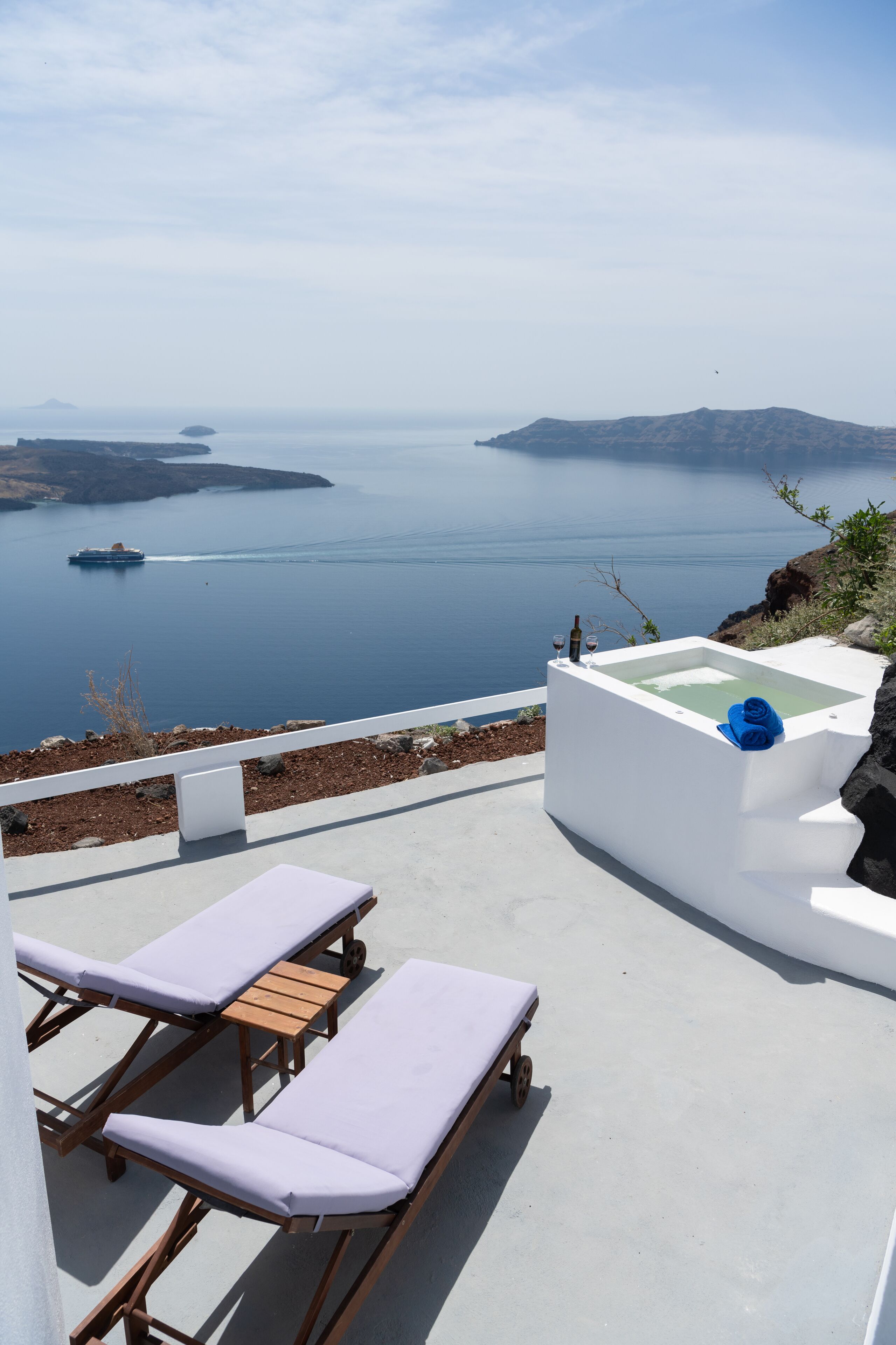 A seaside terrace with lounge chairs and a hot tub overlooking a calm sea and distant islands.