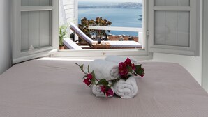 A bedroom with a bed, a window with open shutters, and a view of the sea. - Iatis View Collection (Santorini)