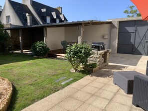 Une terrasse couverte, aménagée avec du mobilier d’extérieur, un barbecue et un mur en pierre.