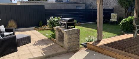 A backyard with a stone barbecue, outdoor furniture, and a wooden deck.