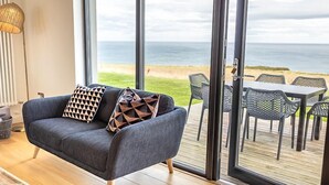 A modern living room with a large window overlooking a beach. - Cottage 15 - 3 Bed (Pwllheli)