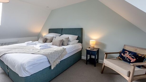 A bedroom with a bed, bedside table, lamp, and chair. - Cottage 15 - 3 Bed (Pwllheli)