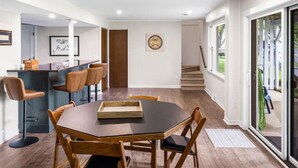 A modern kitchen with a bar area, a dining table with chairs, and a staircase leading to a balcony.