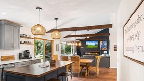 A modern kitchen with a large island, wooden ceiling beams, and pendant lighting.