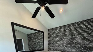 Een moderne woonkamer met een hoekbank, een plafondventilator, een muur met een bakstenen patroon en een houten vloer.