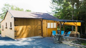 Een houten blokhut met een overdekte patio, een stenen muur en blauwe stoelen.