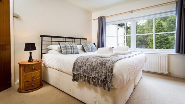 Een slaapkamer met een bed, nachtkastje, lamp en een raam met gordijnen.