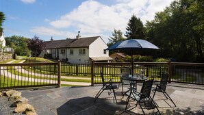 Een terras buiten met een tafel en stoelen, een blauwe parasol en uitzicht op een wit huis met een donker dak.