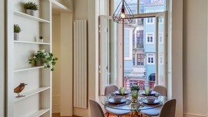 Comedor con mesa de vidrio, sillas y vista a edificios a través de un ventanal.
