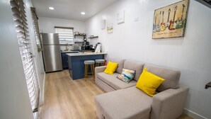 A modern kitchen with a refrigerator, bar stools, and a dining area. - Sunset Villas "Good Morning" Tiny Home Container (Frederiksted)