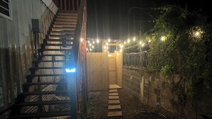 A wooden staircase leading to a wooden door, surrounded by a brick wall and a garden area with string lights. - Sunset Villas "Good Morning" Tiny Home Container (Frederiksted)