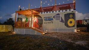 A small, single-story building with a wooden deck and a covered seating area. - Sunset Villas "Good Morning" Tiny Home Container (Frederiksted)