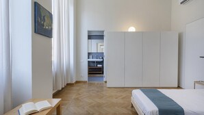 A bedroom with a bed, a bedside table with an open book, a wardrobe, and a bathroom visible through an open door. - Cairoli Stylish Apartment by Wonderful Italy (Genoa)