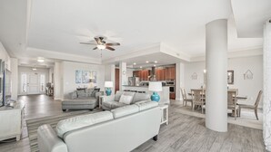 Un soggiorno spazioso con un divano grigio, un'area pranzo con tavolo e sedie, una zona cucina e una ventola a soffitto.