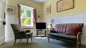 Een woonkamer met een bank, fauteuil, televisie en beelden in lijsten aan de muur.