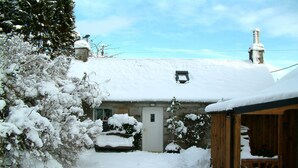 Een besneeuwde cottage met een stenen gevel, een houten veranda en een schoorsteen.