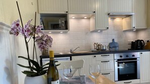Een moderne keuken met witte kasten, een magnetron, een fornuis en een spoelbak. Op het aanrecht staan een fles wijn en twee glazen.