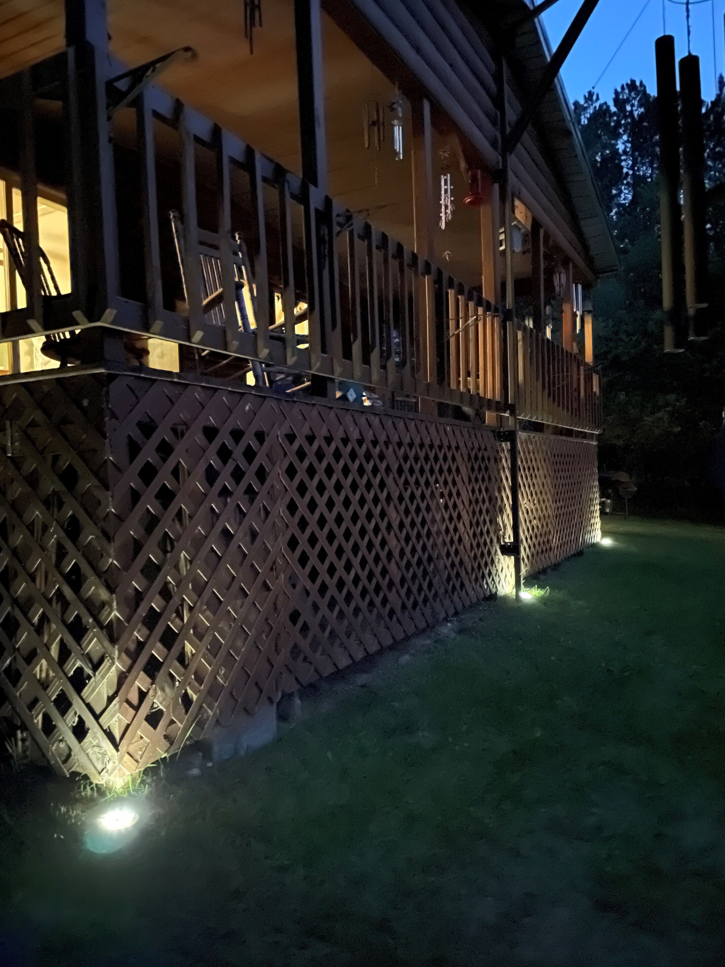 A wooden deck with a lattice fence, a porch with railings, and a building in the background.